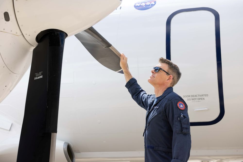 Jon Ohman, who has helped test a variety of engines, including the CFM LEAP***, GEnx, GE9X, and Passport, stands looking up at an aircraft with his hand on the propellor