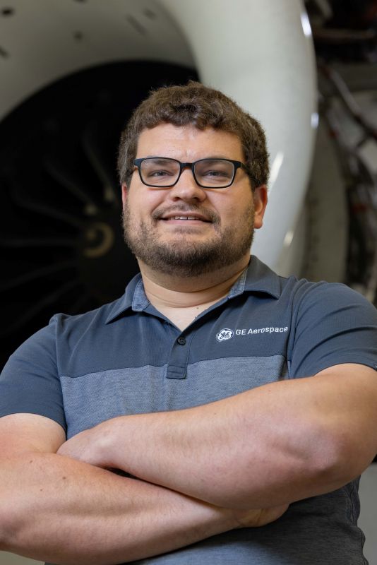 Closeup of a man standing with crossed arms in front of an engine