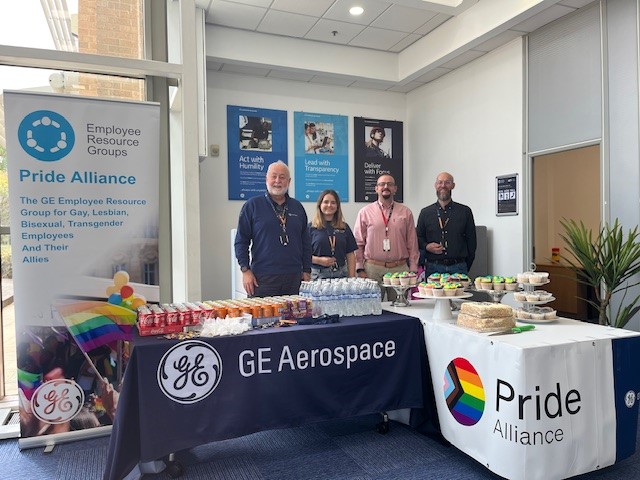 Hywel and his coworkers gather around tables bedecked in GE Aerospace Pride Alliance banners, laden with sodas, waters, and sweet treats.