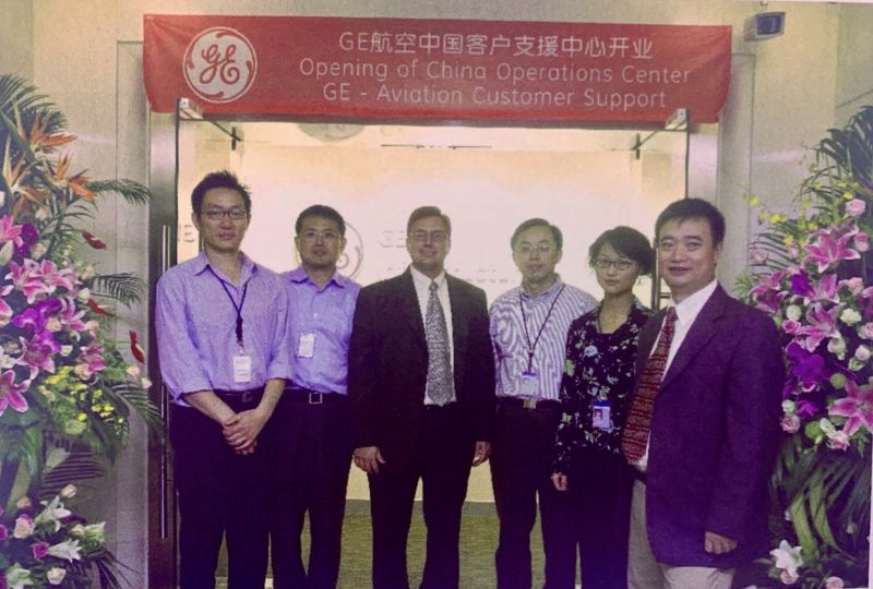 A group of six, five men and one woman, standing beneath a banner for the Opening of GE Aerospace's China Operations Center