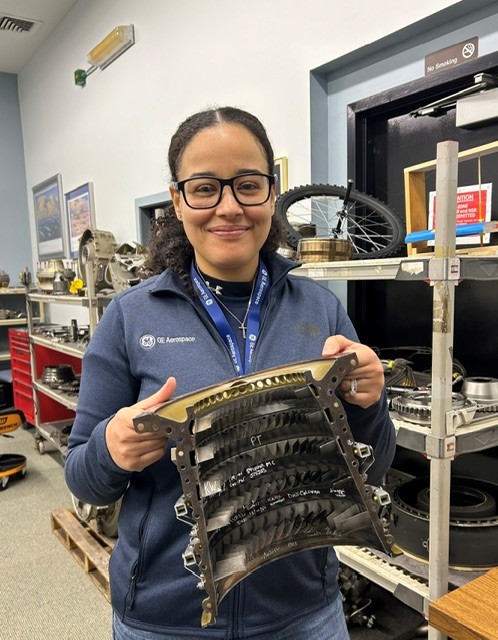 Amber Beebee holds up a mechanical part in a storeroom