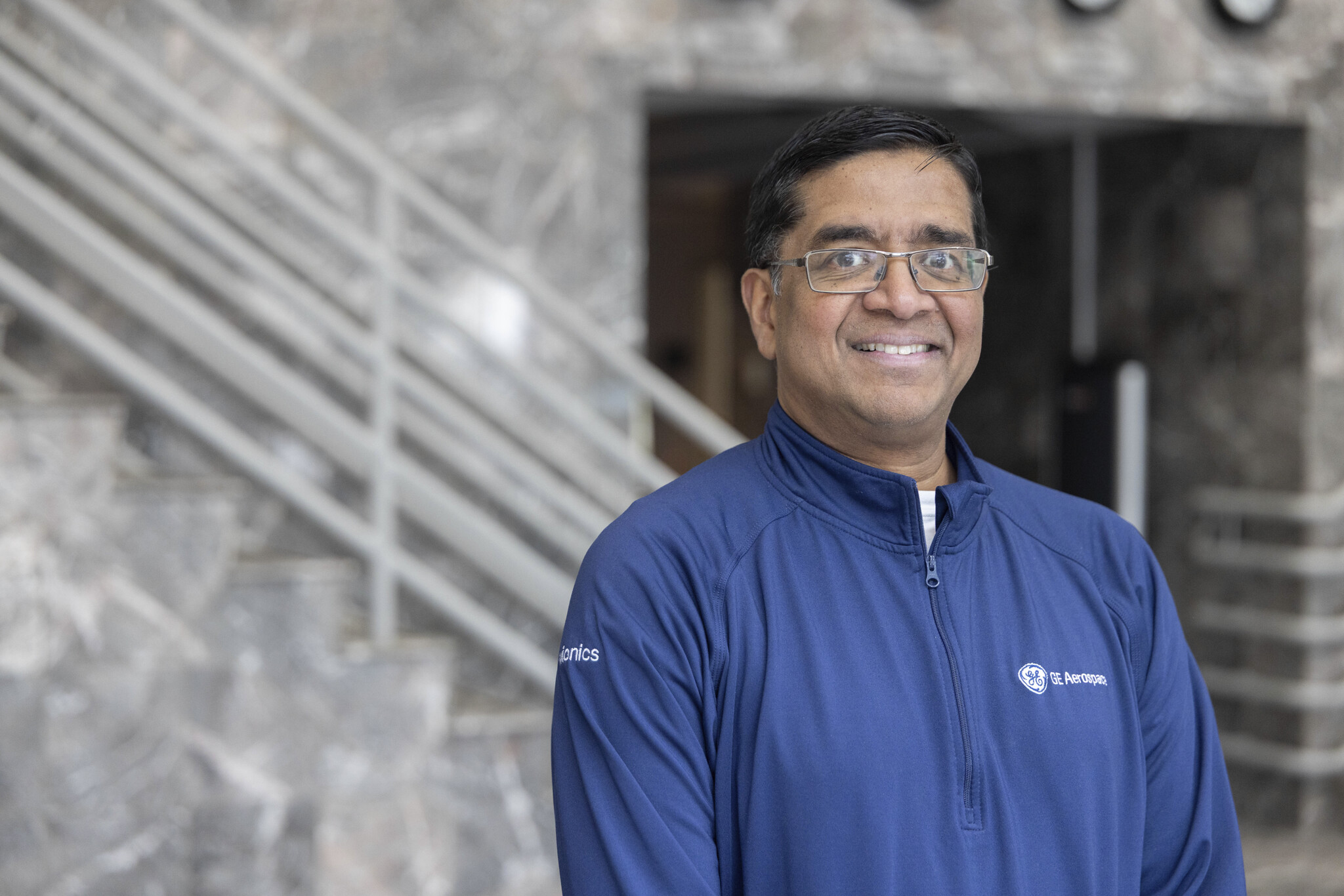 Dev Rajakrishna smiles in a portrait, sporting his blue GE Aerospace zipup