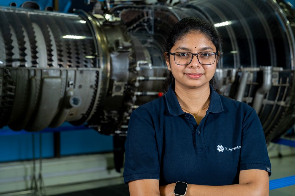 Woman in glasses and a dark blue GE Aerospace polo in front of an engine