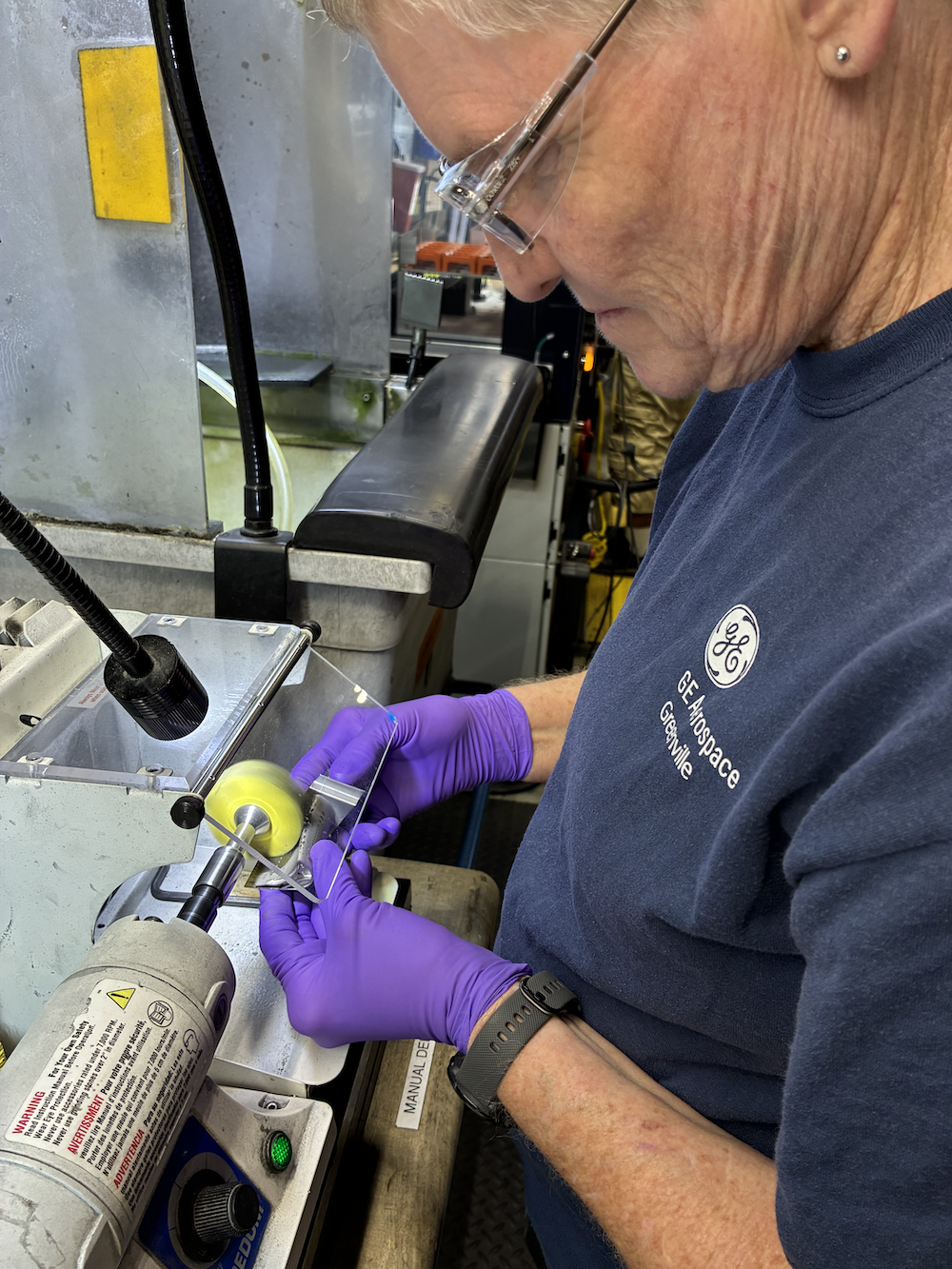 Kim Brady wears safety goggles and gloves as she deburrs a CFM56 blade
