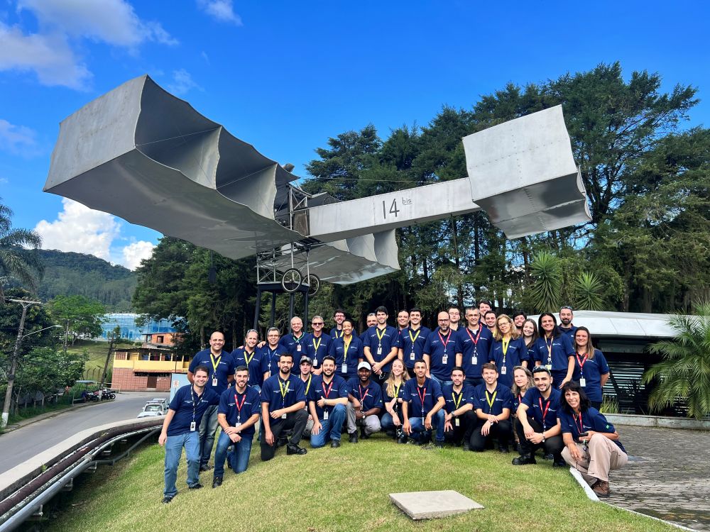 Group of people in blue polos posing outside with an old plane model above their heads