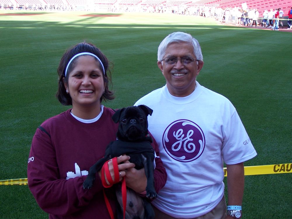 Man and woman holding a small black pug in front of a track field